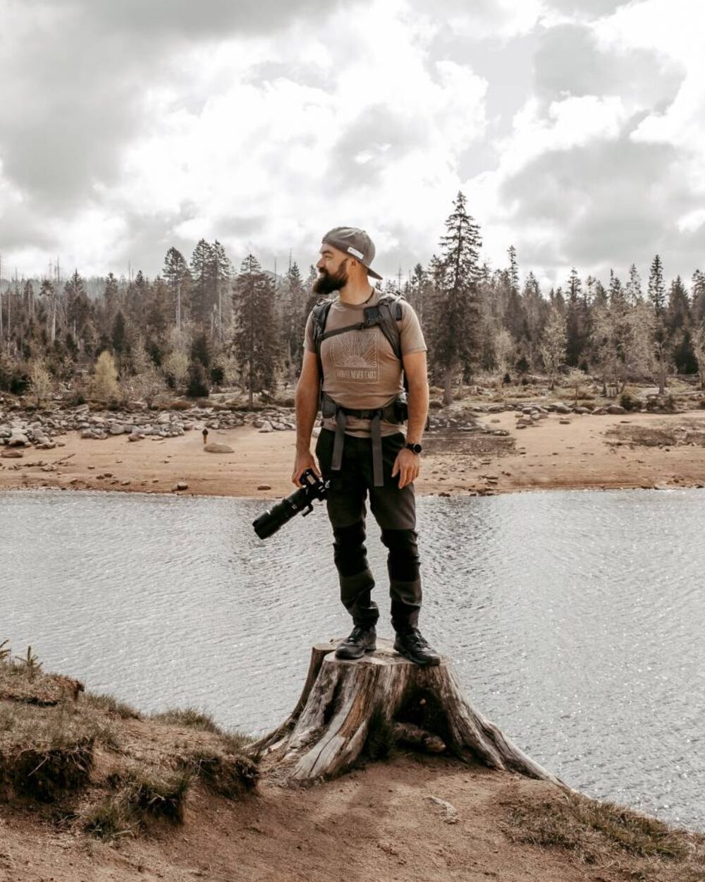 Marvin Rust steht mit Kamera auf einem Baumstumpf am See im Harz
