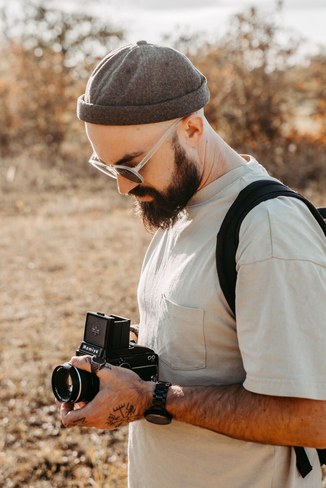 Marvin Rust mit Mütze und Sonnenbrille schaut auf seine analoge Mamiya, im Hintergrund ein goldenes Feld