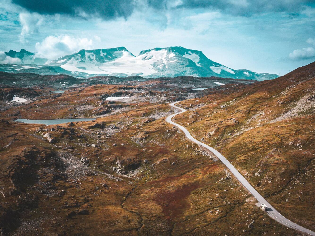 Straße durch eine rotbraune Hochebene vor Gletscherbergen in Norwegen