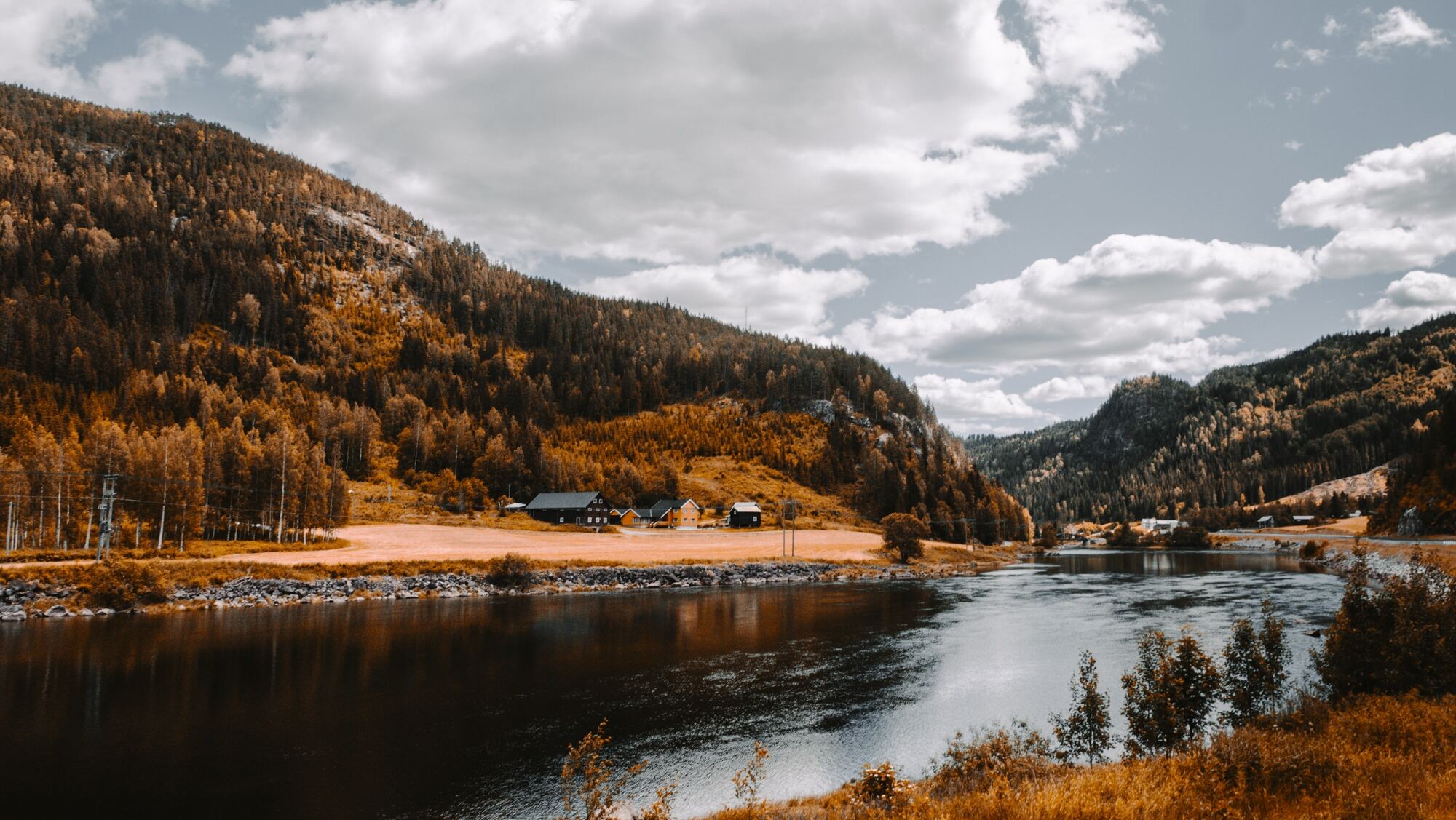 Herbstliches Tal mit Fluss unter weißen Wolken