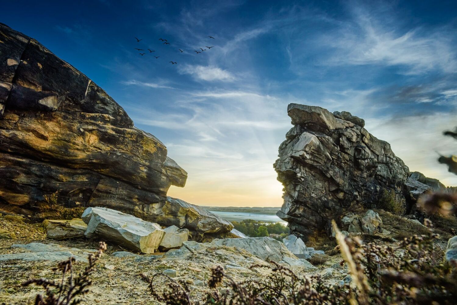 Zwei Felsen der Teufelsmauer rahmen den Blick ins Tal, Vogelschwarm im Abendhimmel