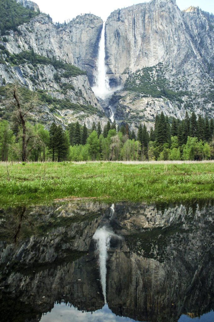 Hoher Wasserfall an einer Felswand spiegelt sich in einem stillen See